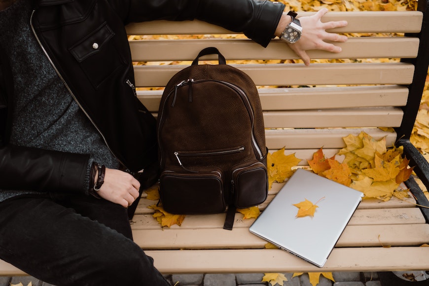 A man sitting on a bench with a backpack and laptop.