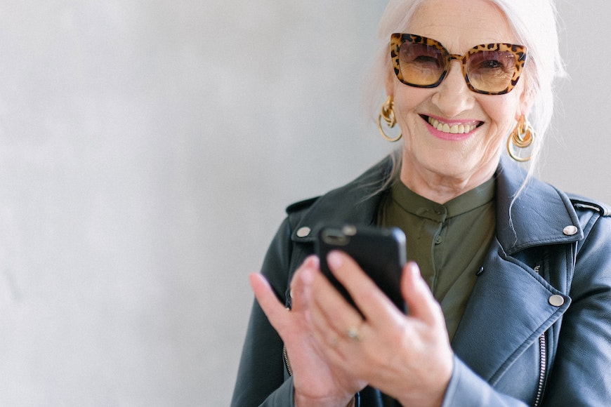 An older woman wearing sunglasses and a leather jacket looking at her phone.