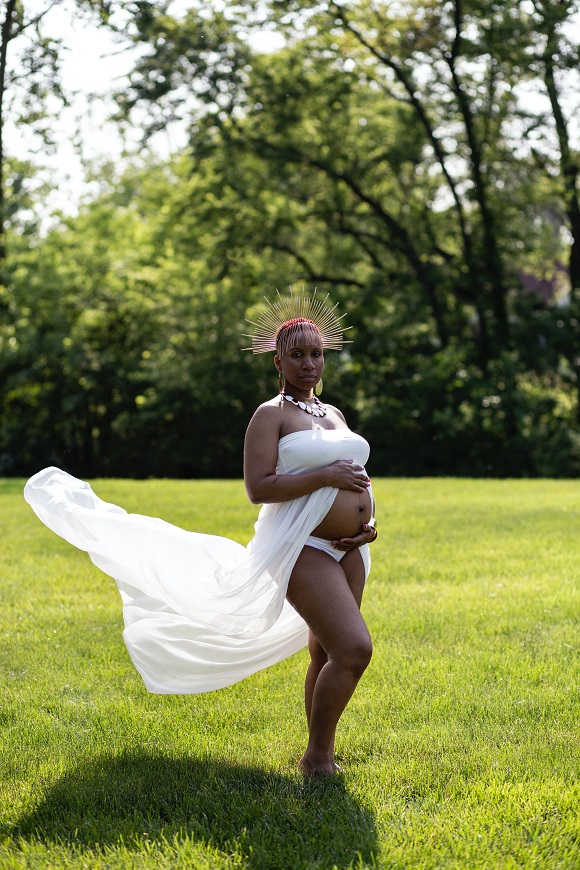 A pregnant woman in a white dress posing in the grass.