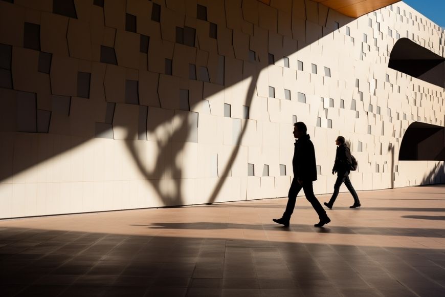 Two people walking in front of a building with shadows.