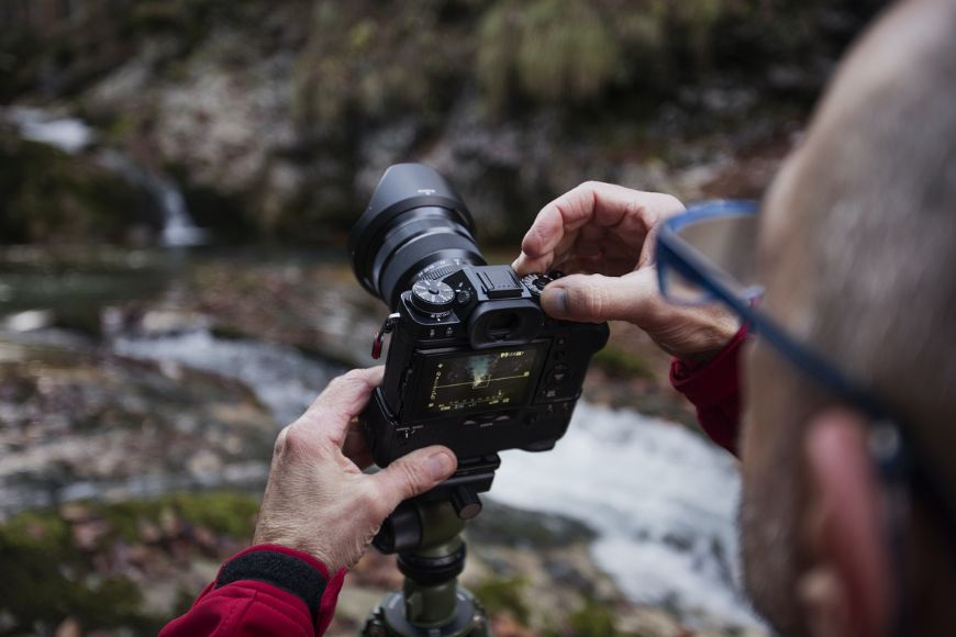 A man holding a camera in front of a waterfall.