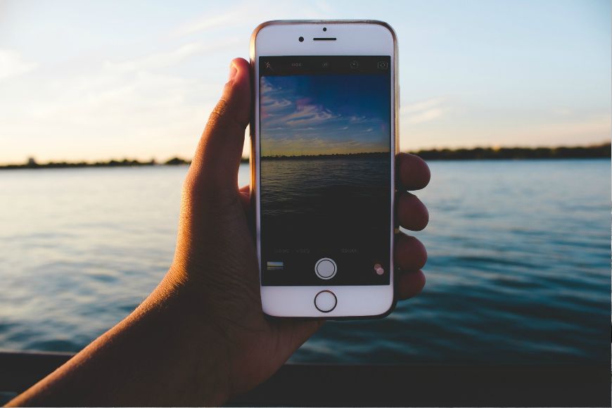 A person holding up an iphone in front of a body of water.