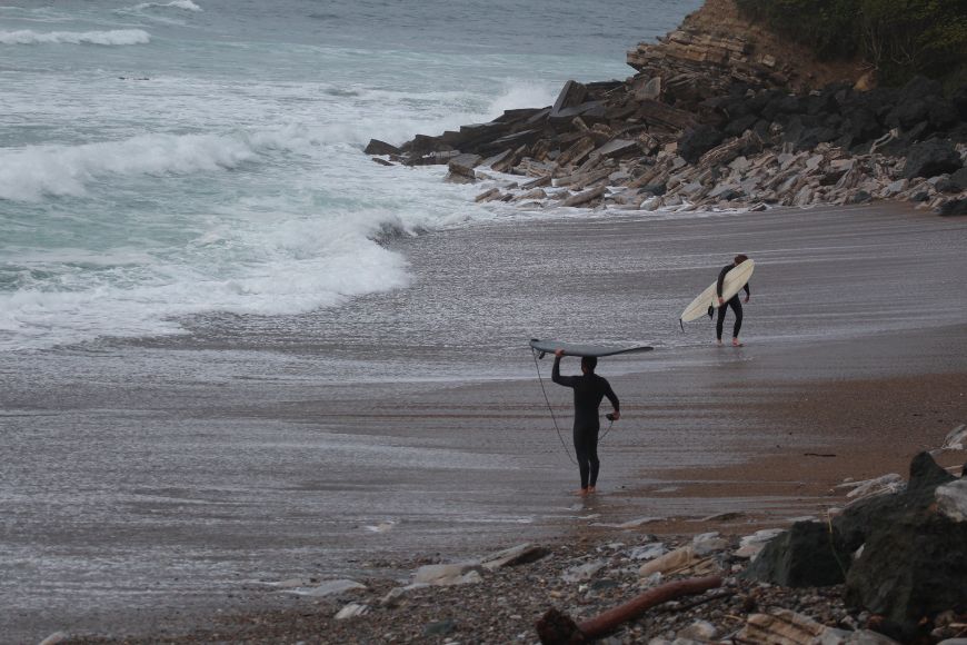 A group of people walking along a beach with surfboards.
