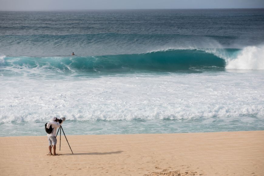 A man is taking a picture of a wave in the ocean.