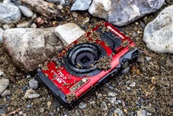 An OM System TG-7 camera is laying on a rock in the mud.