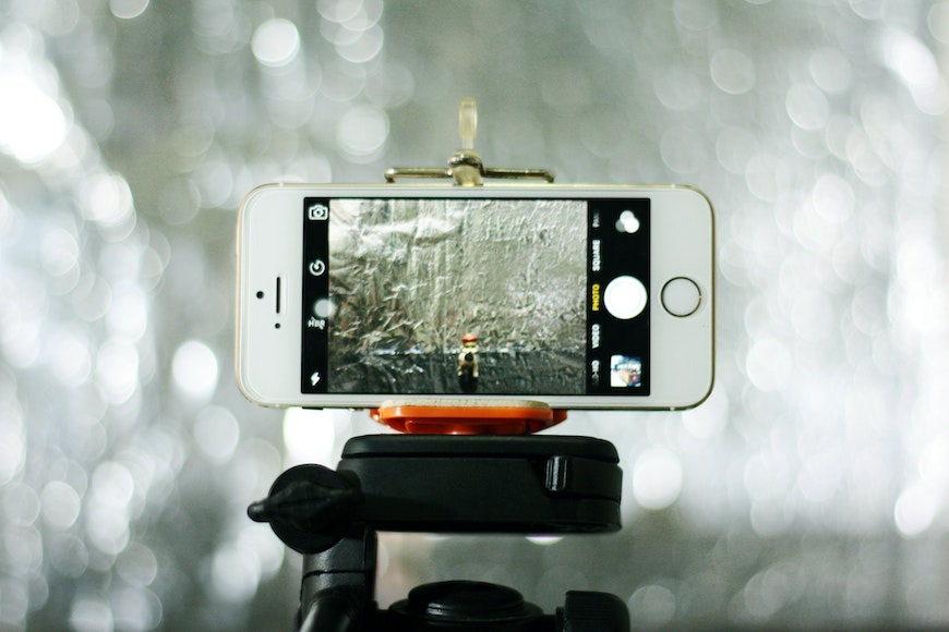 A cell phone on a tripod in front of a mirror.