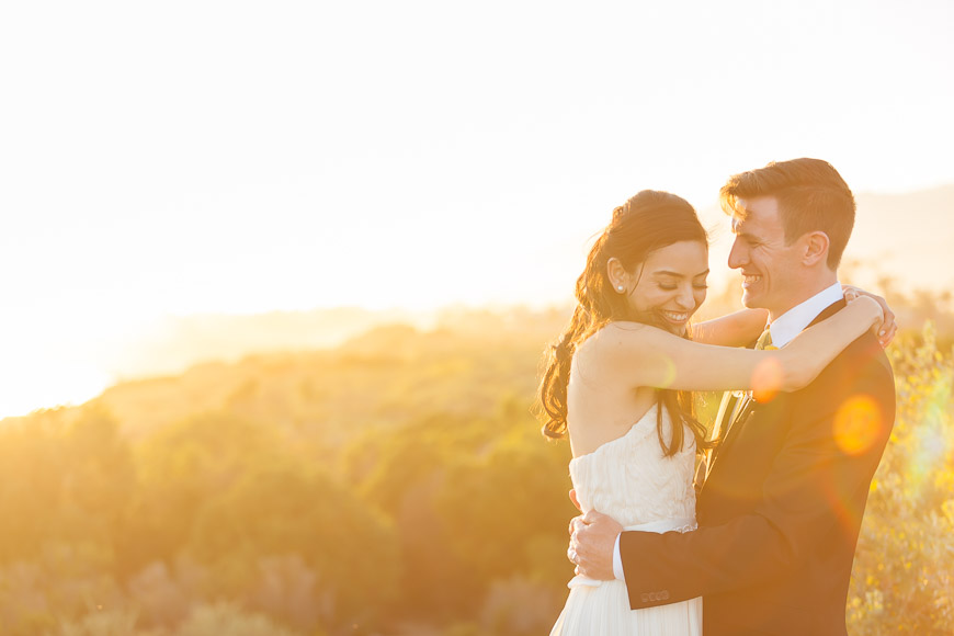 A bride and groom embrace at sunset in california.