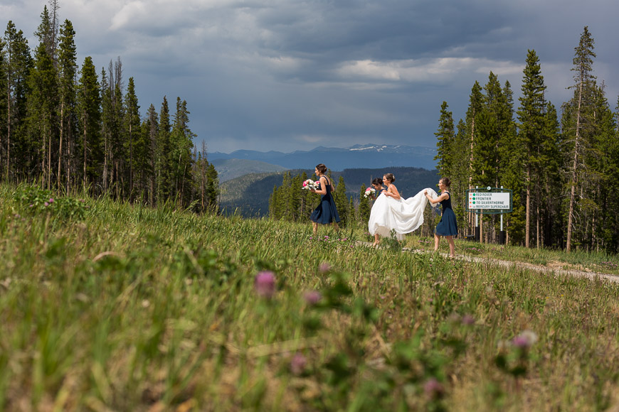 A bride and her bridesmaids walk down a path in the mountains.