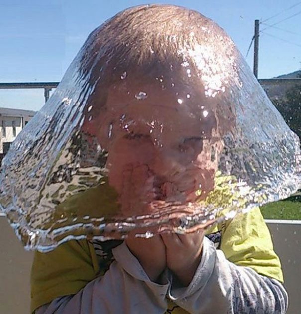 A young boy with a hat covered in water.