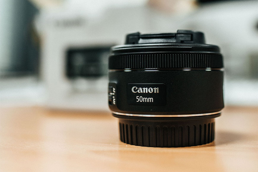 A canon eos 50mm f/1.8 lens sits on a table.
