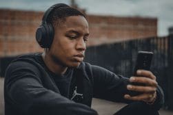 A young man wearing headphones and looking at his phone.
