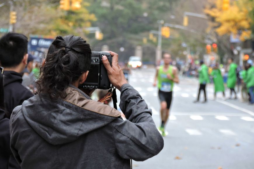 A person taking a picture of a person running in a marathon.