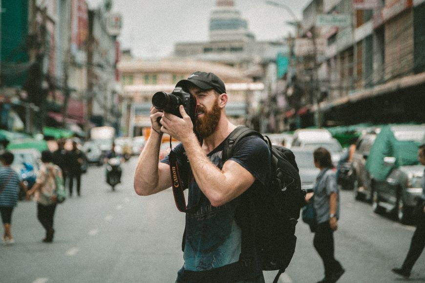 A man with a beard taking a picture of a city street.