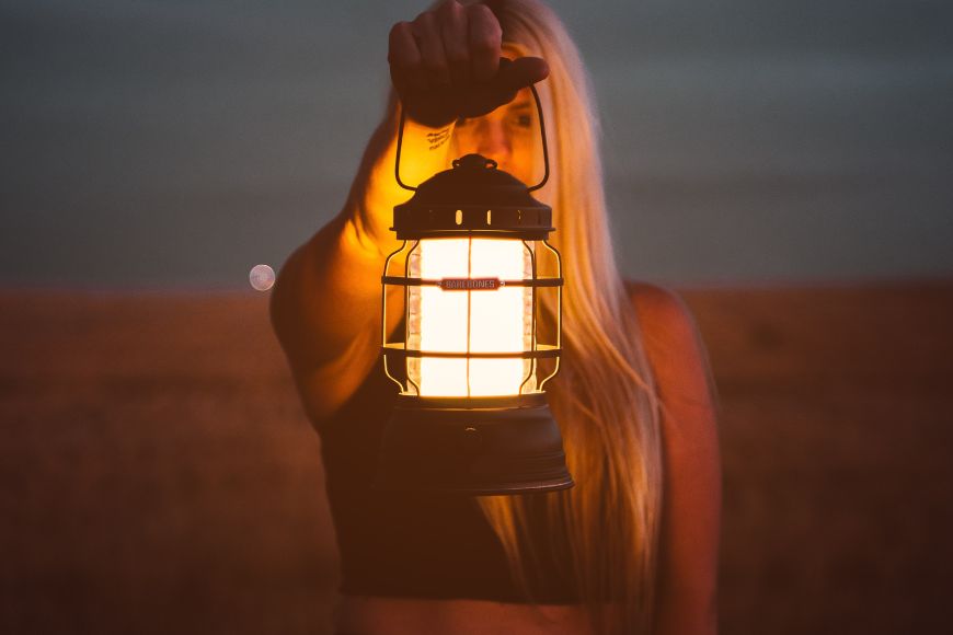 A woman holding a lantern in the middle of a field.