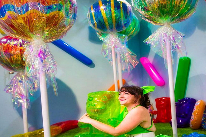 A woman in a green dress sits on top of a giant lollipop.