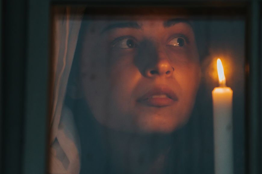 A woman looking out of a window with a candle in her hand.