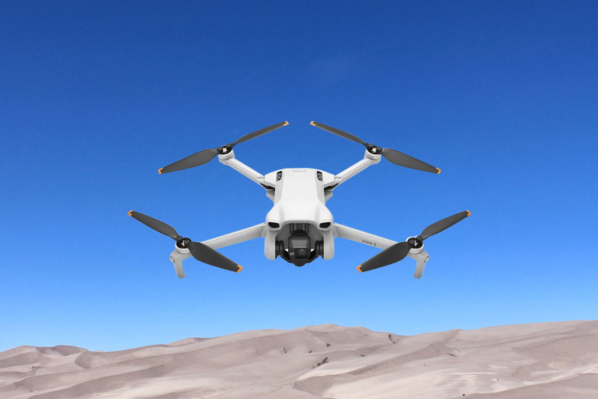A white drone flying over a desert.
