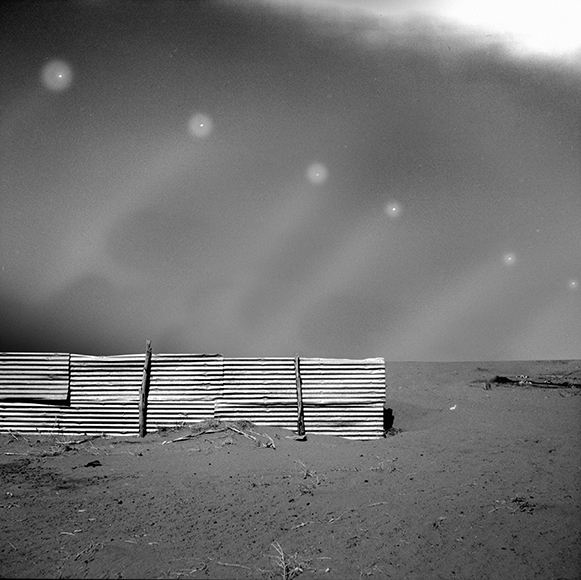 A black and white photo of a fence in the desert.