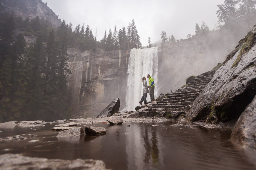 A man and a woman standing near a waterfall in yosemite national park.