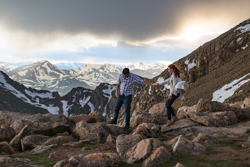 A couple walking on rocks in the mountains during their engagement session.