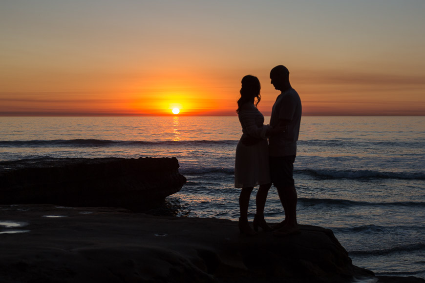 A couple standing on a rock at sunset.