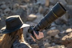 A woman wearing a hat and holding a large lens.