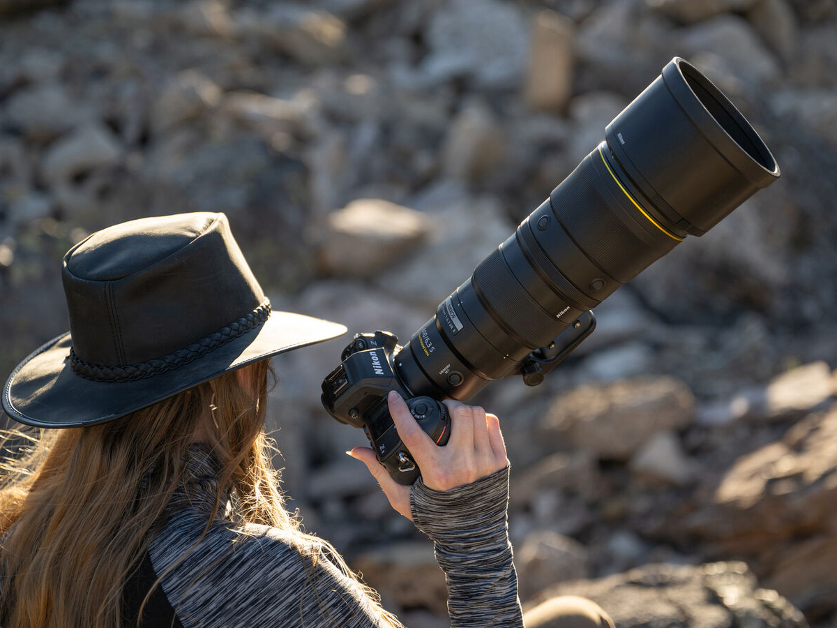 A woman wearing a hat and holding a large lens.