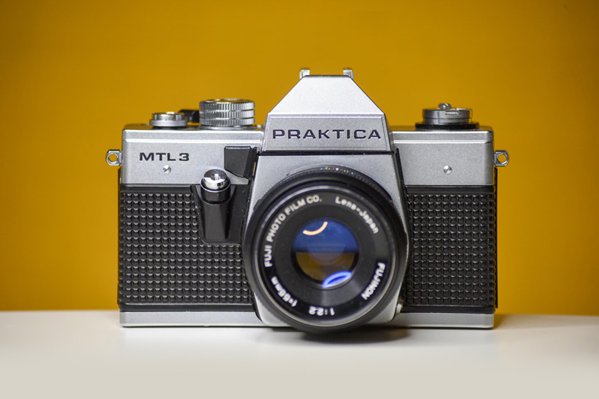 A silver camera sits on a yellow background.