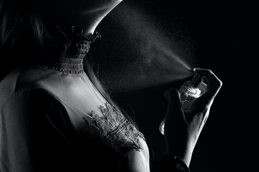 A black and white photo of a woman spraying perfume.