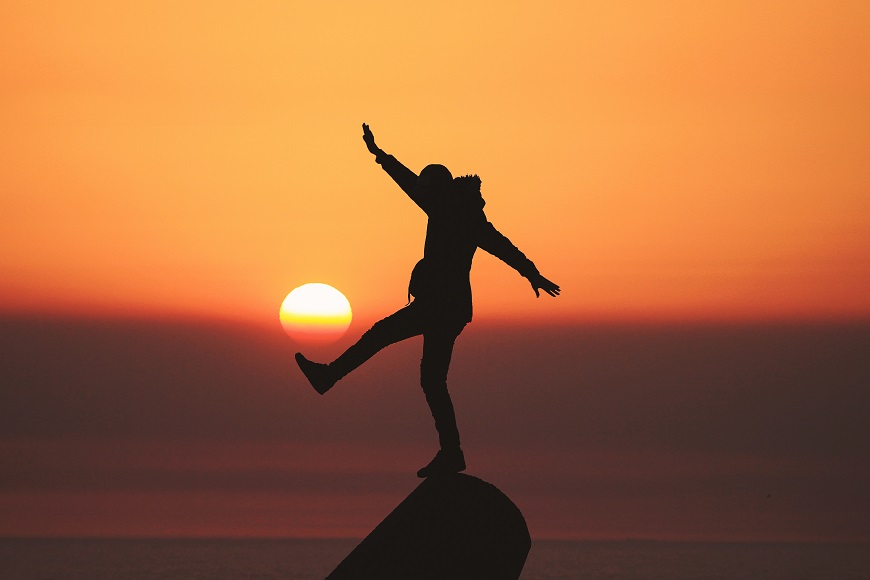 A silhouette of a person standing on top of a rock at sunset.