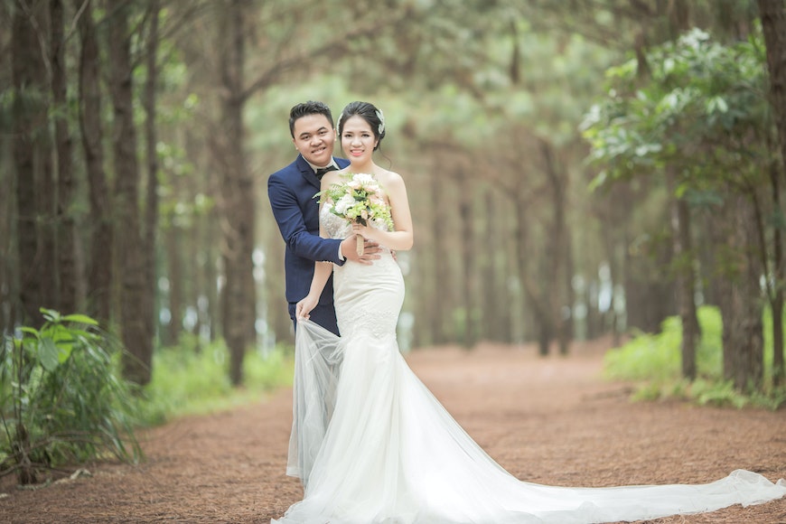 A bride and groom posing in a wooded area.