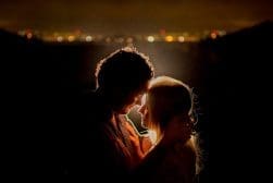 A couple embracing in front of a city at night.