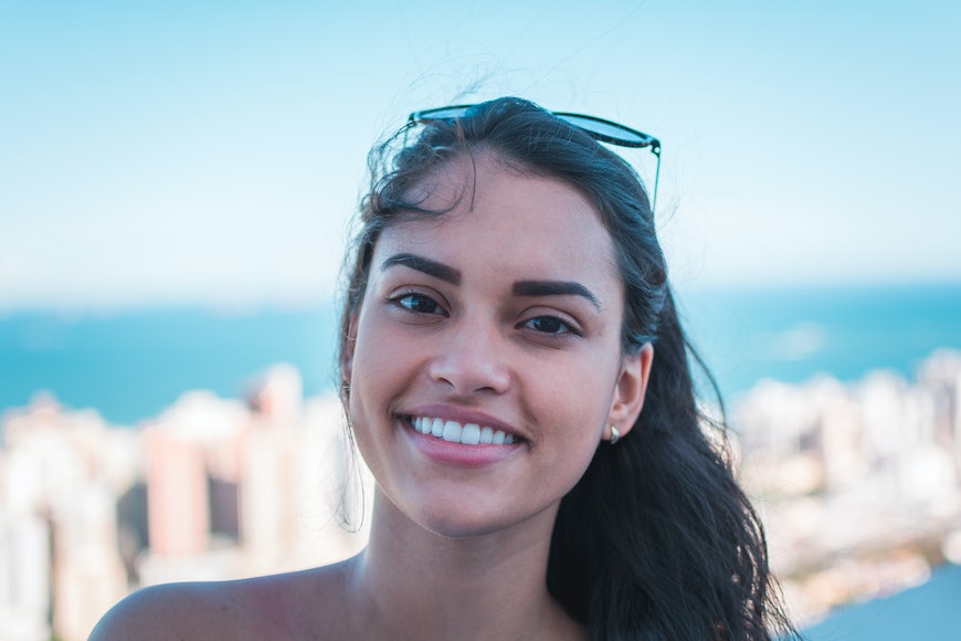 A young woman smiling at the camera in front of a city.