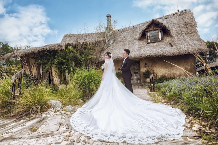 A bride and groom standing in front of a thatched house.
