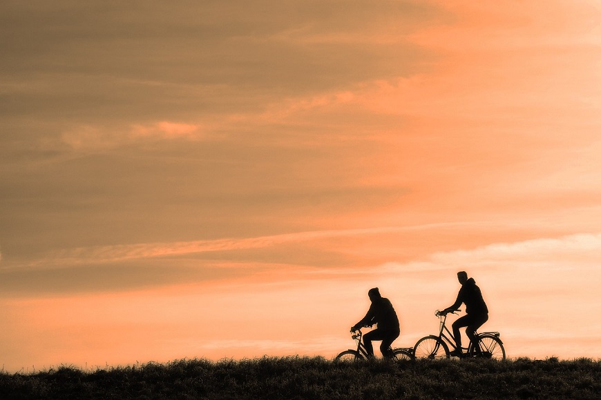 Two people riding bicycles on a hill at sunset.
