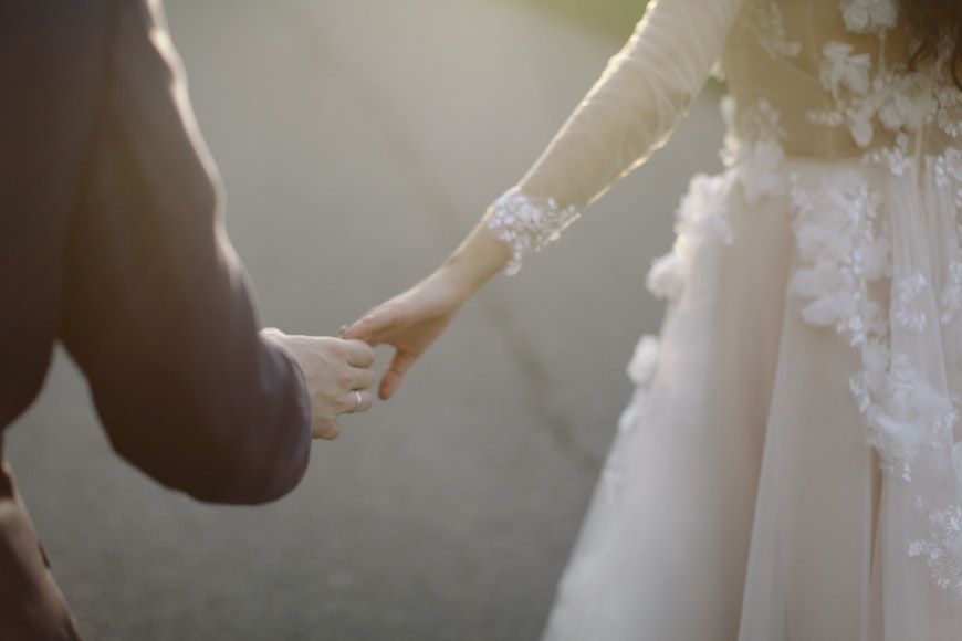A bride and groom holding hands on a road.