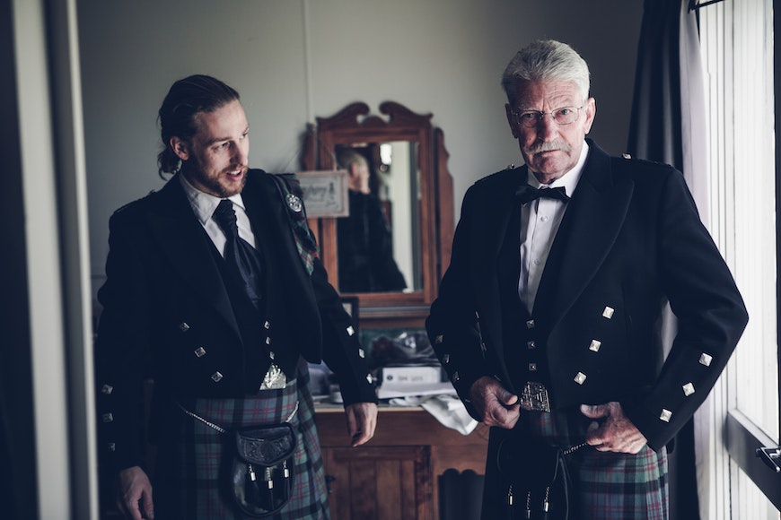 Two men in kilts standing in front of a mirror.