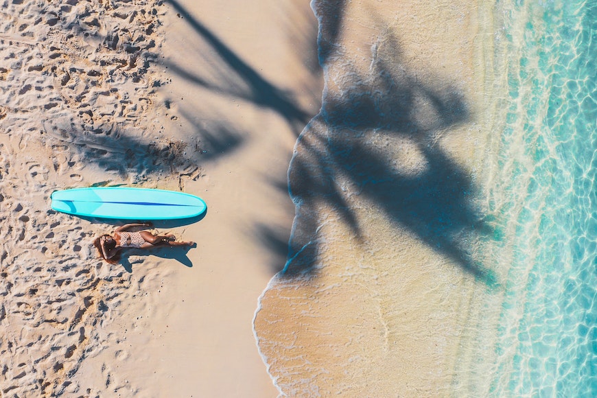 A woman is laying on the beach with a surfboard.