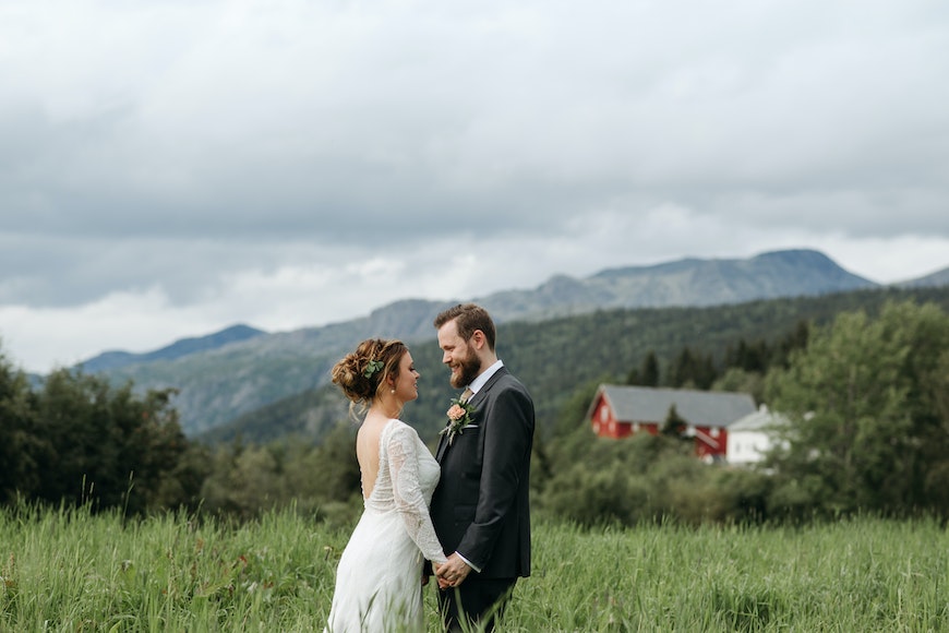 A bride and groom standing in a field with mountains in the background.