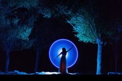 A woman in a dress standing in front of a circle of light.