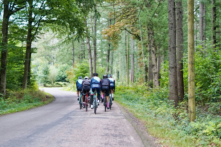 A group of cyclists riding down a road in a wooded area.
