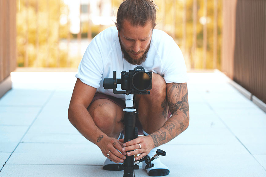 A man crouching down with a camera on a tripod.