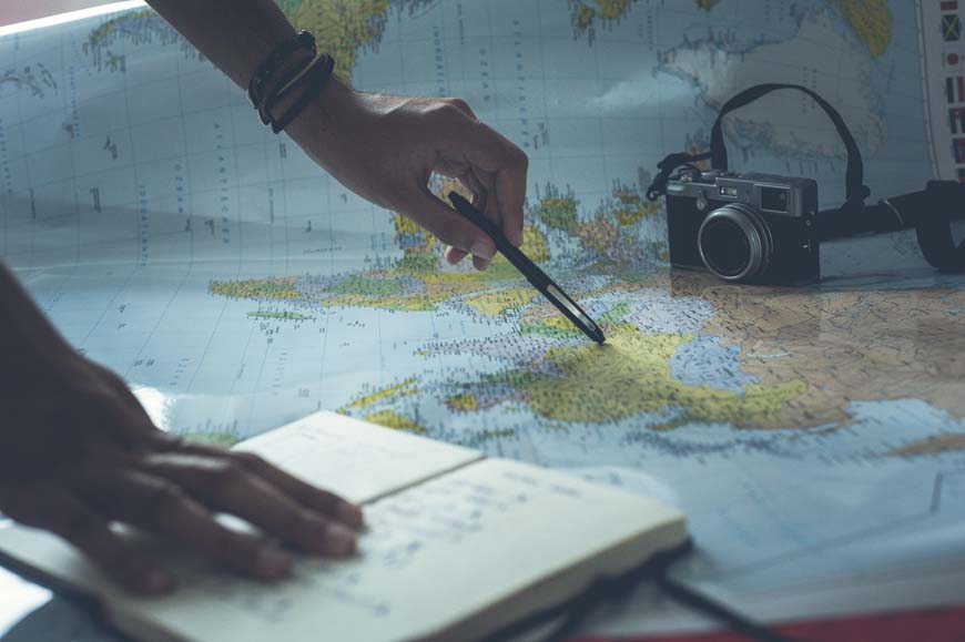 A person holding a camera and a notebook on top of a map.