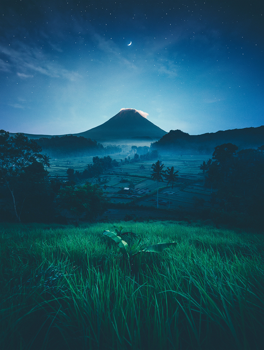 An image of a mountain and a green field at night.