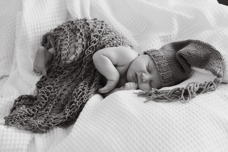 A black and white photo of a baby sleeping on a blanket.
