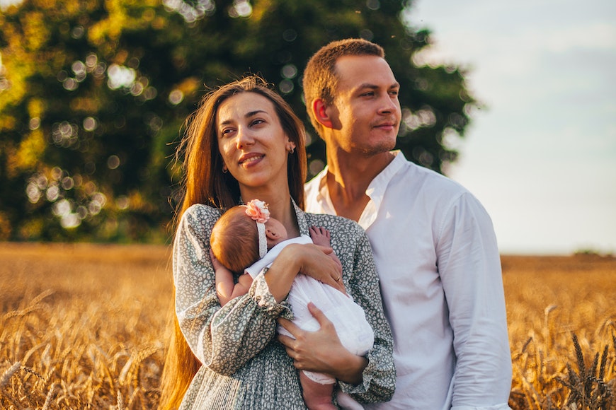 A couple holding a baby in a wheat field.