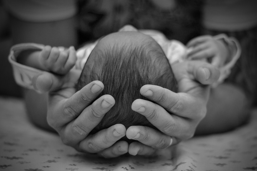 A black and white photo of a person holding a baby's head.