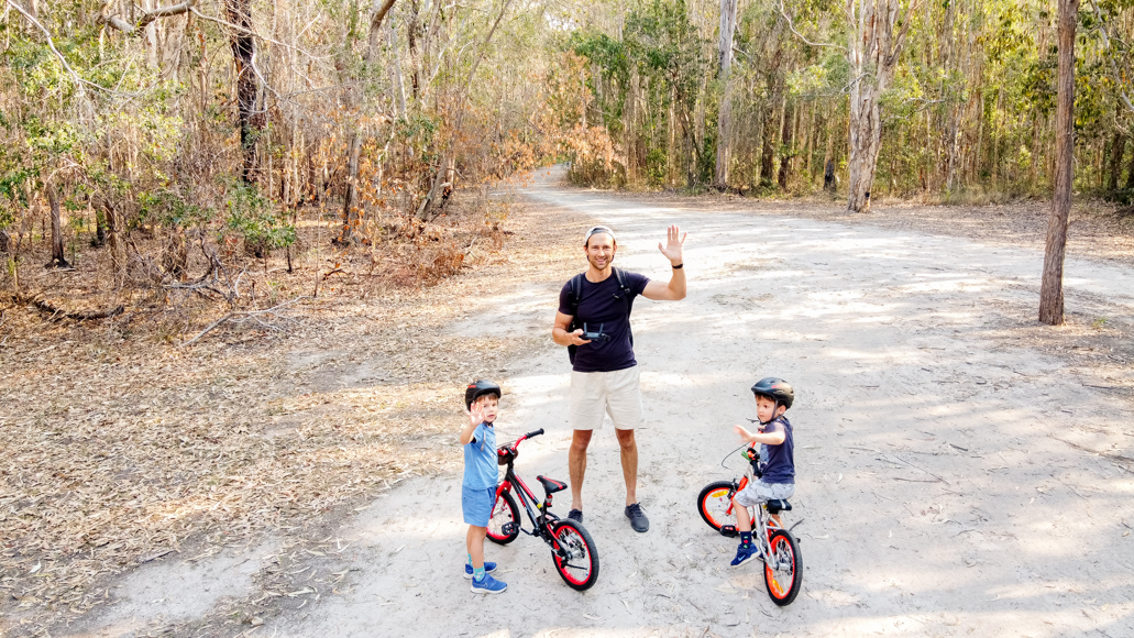 A man and two boys standing on a dirt road with their bikes.