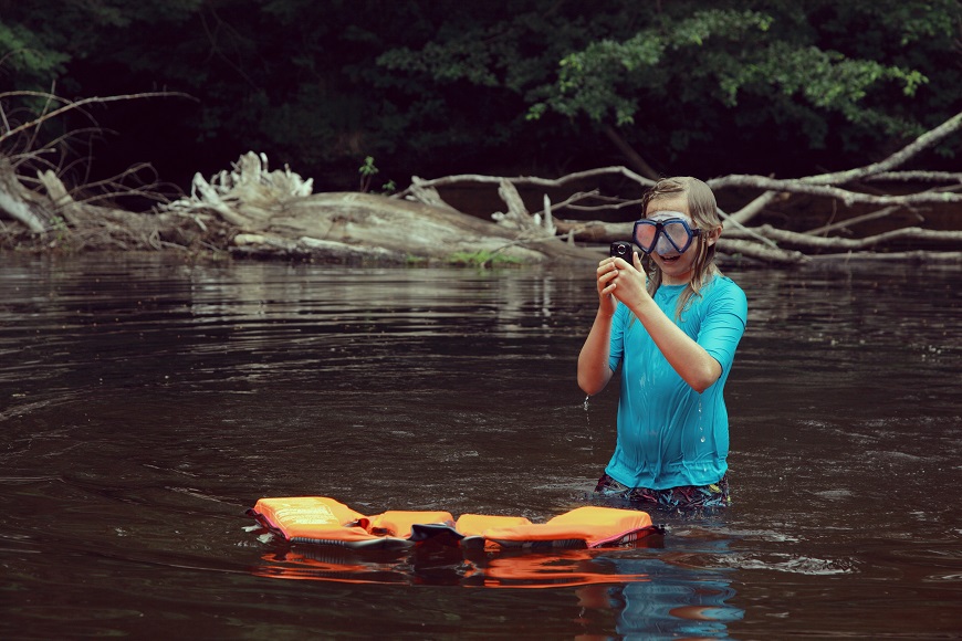 A girl is standing in a river with a life jacket.
