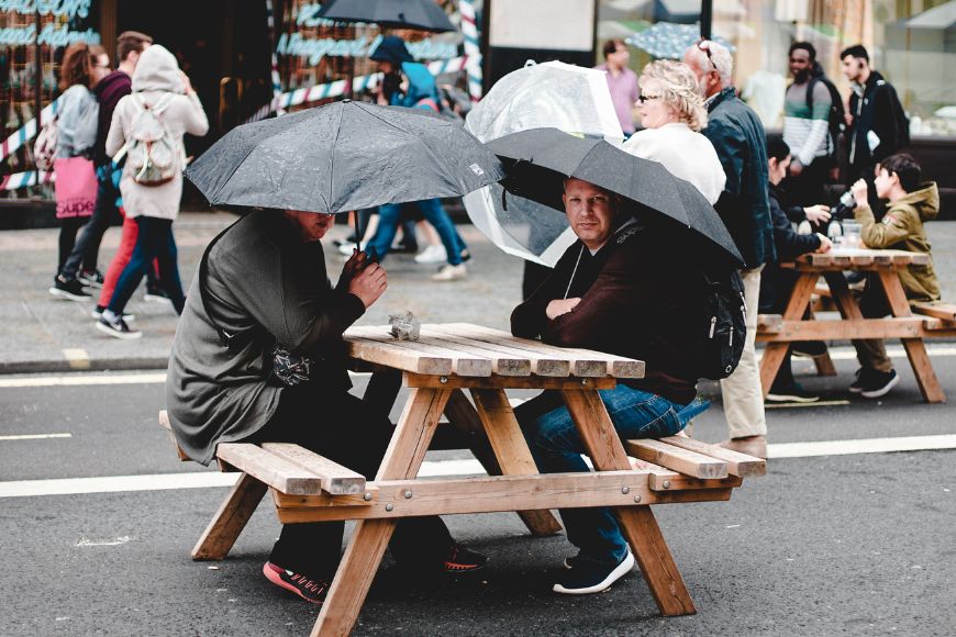 Two people sitting at a picnic table under umbrellas.